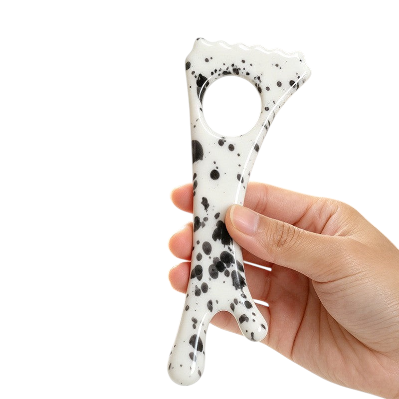 The Tailored Tail ceramic pet massage stick with a white and black speckled pattern held in a hand
