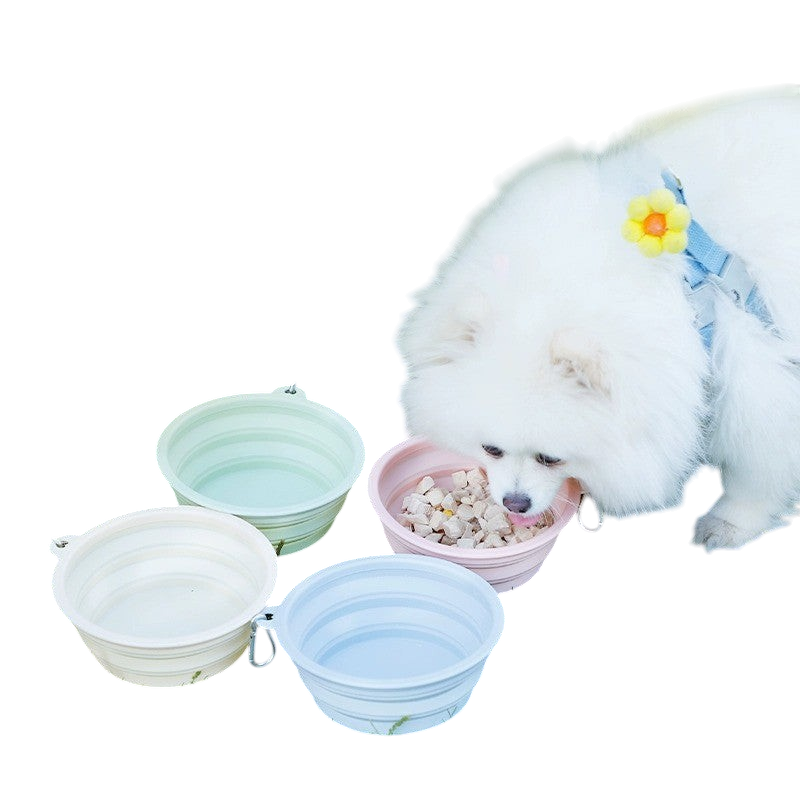 A fluffy white dog eating from a pink The Tailored Tail foldable silicone pet bowl on a grassy lawn.