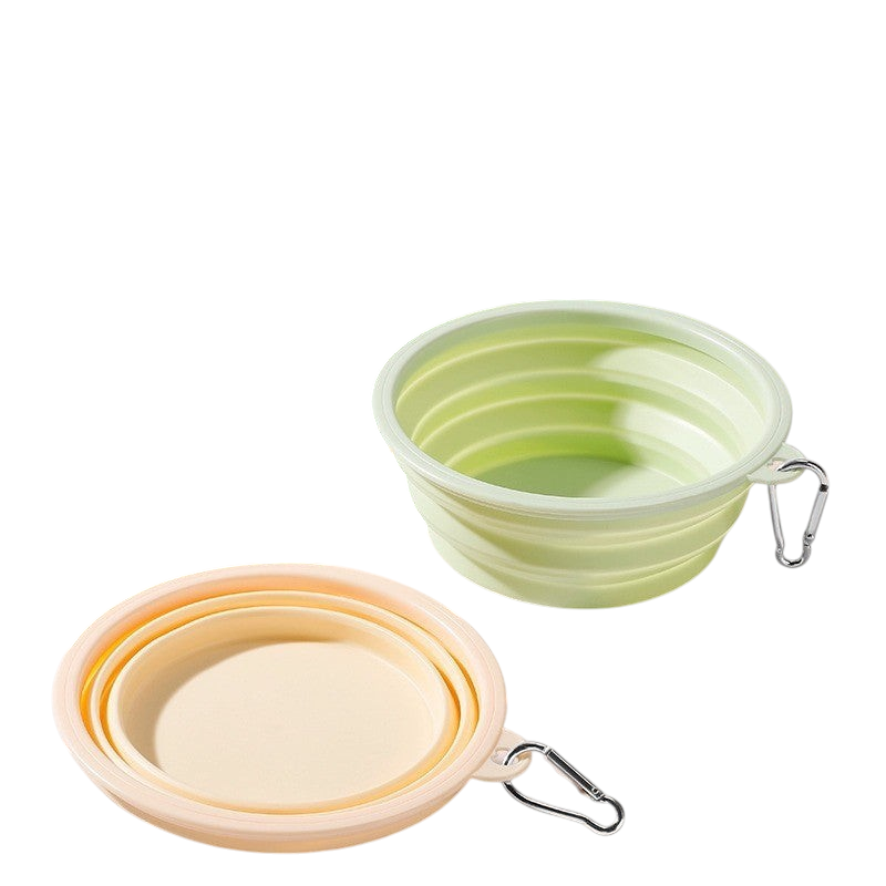 The Tailored Tail foldable silicone pet bowls in green and yellow with carabiner clips for travel on a wooden surface.